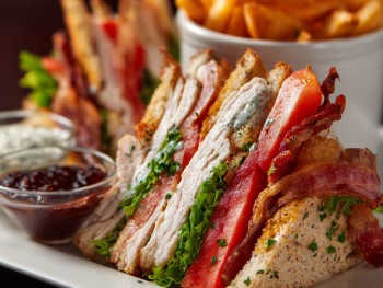 Three layers, triple-decker, always toasted. Turkey, bacon, ham, Swiss, lettuce, tomato, and mayo on toasted white bread. Held together with frilled toothpicks because presentation matters.